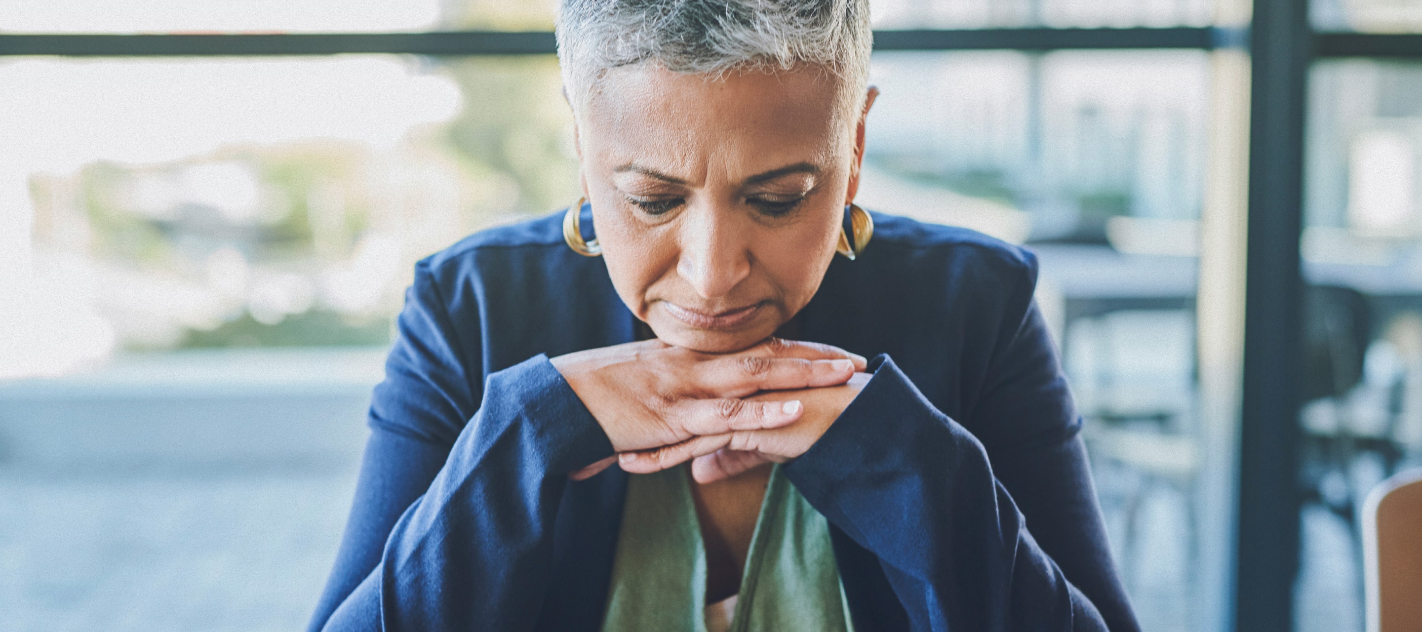 Woman resting her chin on her hands, looking down with serious expression on her face