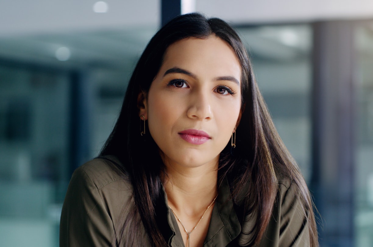 Pensive woman sitting in an office setting, looking at the viewer.