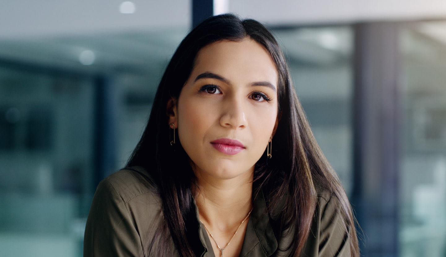 Pensive woman sitting in an office setting, looking at the viewer.